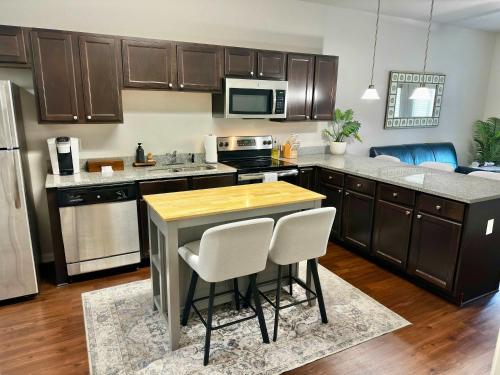 a kitchen with wooden cabinets and a kitchen island with white chairs at Walk to Stadium & Cotton District, Balcony & Pool in Starkville