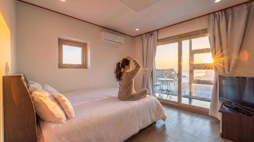 a woman sitting on a bed in a bedroom with a window at Samcheok jangho sanho Pension in Samcheok