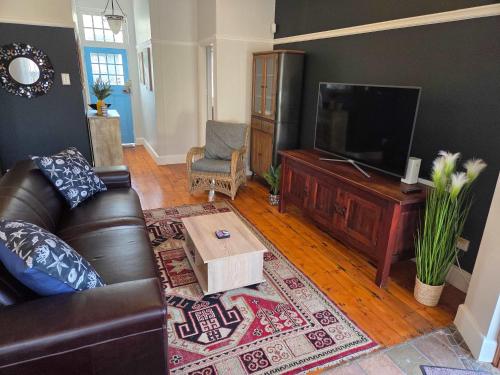 a living room with a leather couch and a flat screen tv at Beach Street Self-Catering in Mossel Bay