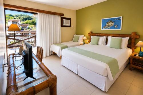 two beds in a room with a tv and a balcony at Rio Búzios Beach Hotel in Búzios