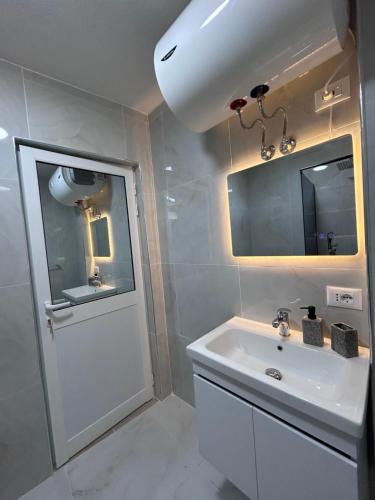 a white bathroom with a sink and a mirror at Bujtina e Qilimave in Zogaji