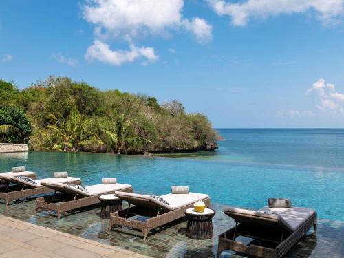 a swimming pool with lounge chairs and the ocean at Raffles Bali in Jimbaran