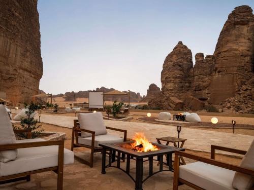 a patio with chairs and a fire in front of some rocks at Shaden Resort Al Ula, Managed by Accor in Al-ʿUla