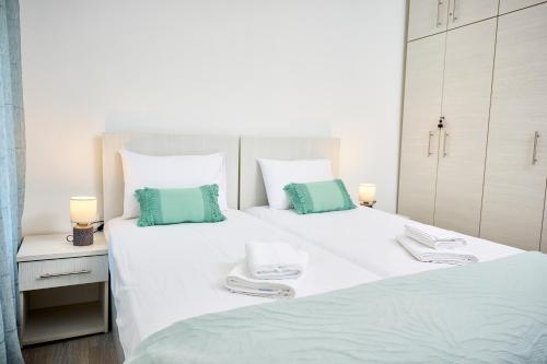 a white bedroom with two beds with green and white pillows at Casa di Fava in Agios Nikolaos