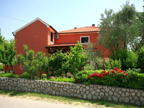 a red house with a stone wall in front of a garden at Rooms Nadica in Baška