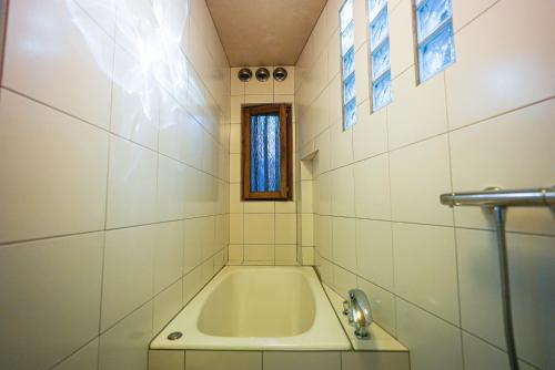 a bath tub in a white tiled bathroom with a window at Moon's Cafe in Onomichi