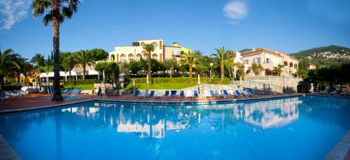 une grande piscine bleue avec des palmiers et des bâtiments dans l'établissement Residence Pian Dei Boschi, à Pietra Ligure