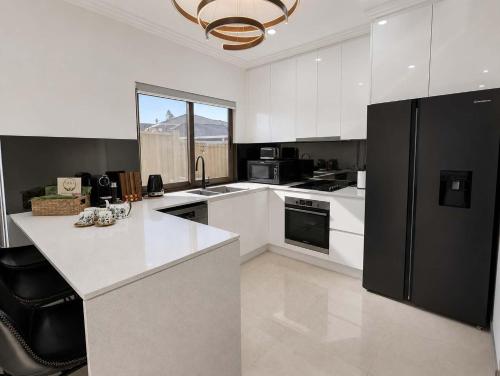 a kitchen with white cabinets and a black refrigerator at Cara Luxe Stays at Regents Park near Olympic Park and DFO in Regents Park