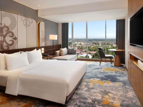 a bedroom with a large white bed and a living room at Mercure Pangkalan Bun in Pangkalan Bun