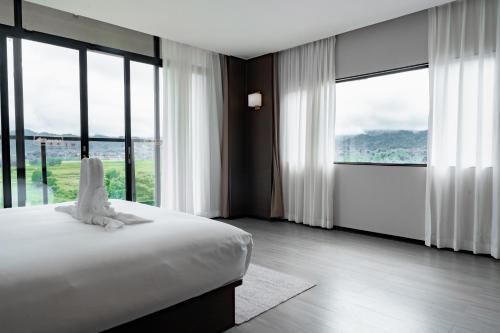a bedroom with a white bed and large windows at Vangvieng THAVIKUN HOTEL in Vang Vieng