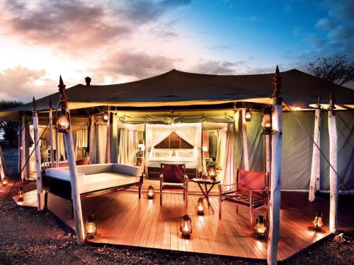 a tent with a bed and a chair on a deck at One Nature Nyaruswiga Serengeti in Banagi
