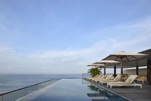 a pool with chairs and umbrellas next to the ocean at Alila Seminyak in Seminyak