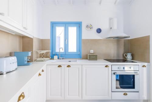 a kitchen with white cabinets and a blue window at Maison Mariel in Skopelos Town