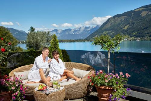two people in white robes sitting on a patio with a view of a lake at Grand Hotel Zell am See in Zell am See