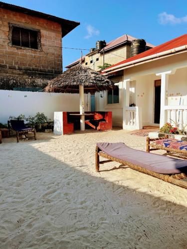 a bed on the beach next to a building with an umbrella at Meama Paje Guesthouse in Paje