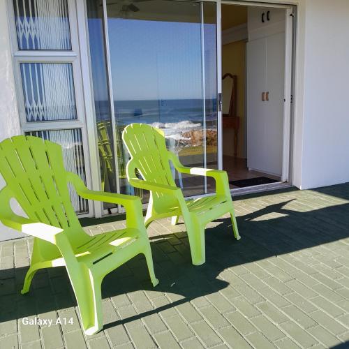 two green chairs sitting on a balcony with the ocean at ROMANZA APARTMeNT in De Kelders