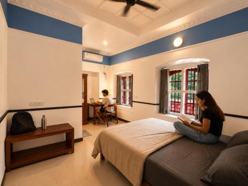 a woman sitting on a bed reading a book at Hope Hostels, Fort Kochi in Fort Kochi