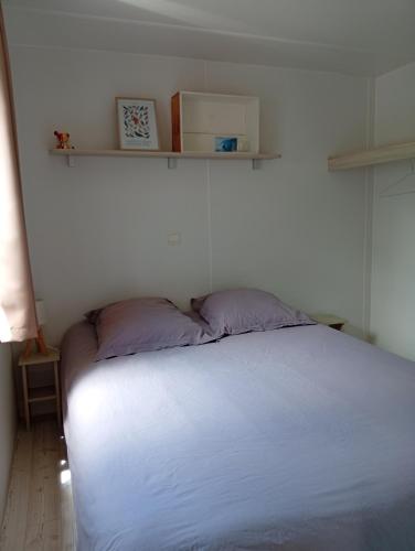 a bedroom with a white bed with two purple pillows at FH Mobile home Camping des Viviers in Lège-Cap-Ferret