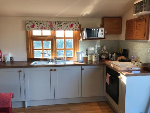 a kitchen with white cabinets and a sink and a window at Garden Studio for Two in Doune