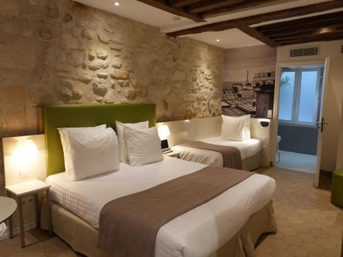 a bedroom with two beds and a stone wall at Hôtel De La Herse d'Or in Paris