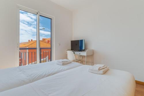 a white bedroom with two beds and a window at Esfera I Calm Stay With Parking & Workspace in Caniço