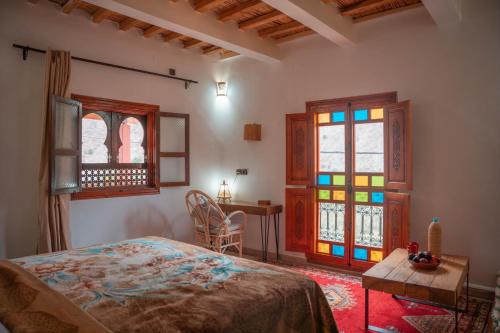 a bedroom with a bed and a table and windows at Ijoukak Berber HomeStay in Ijjoukak