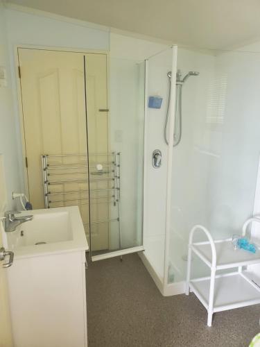 a white bathroom with a shower and a sink at Rawhiti Cottage at Kaeppeli's in Kuaotunu