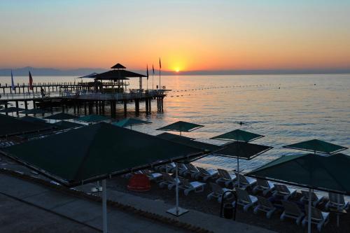 a beach with umbrellas and a pier at sunset at Seagull Hotel in Beldibi