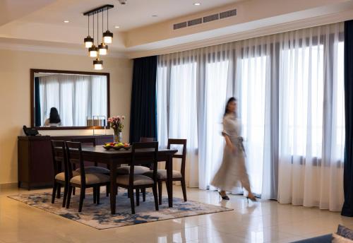 a woman walking through a living room with a table at Sedra Arjaan by Rotana in Doha
