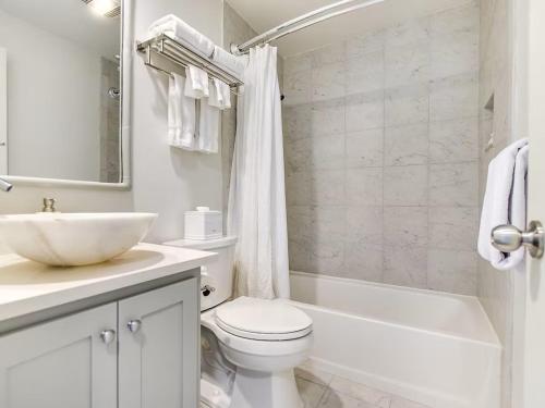 a white bathroom with a sink and a toilet and a tub at Lakefront Treehouse on Lake Travis Pool & Hot Tub in Lakeway