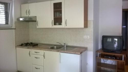 a kitchen with white cabinets and a sink and a tv at Apartments Jurjevic in Petrcane