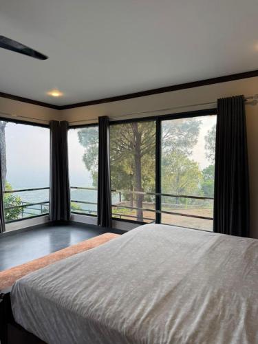 a bedroom with a large bed and large windows at Baam-E-Noor , Pine Tree Resort , Margalla Hills Islamabad in Harīpur