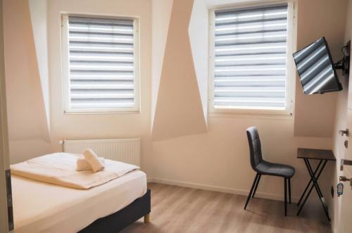 a bedroom with a bed and a chair and two windows at Hotel Gasthaus Krone in Cologne