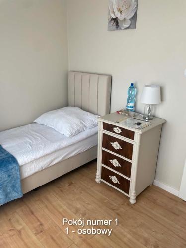 a bedroom with a bed and a dresser with a lamp at Rubinkowo Rooms Self Check-in 24h in Toruń