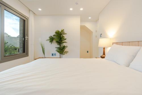 a white bedroom with a large bed and a window at 제주살랑 in Tŏksu-dong