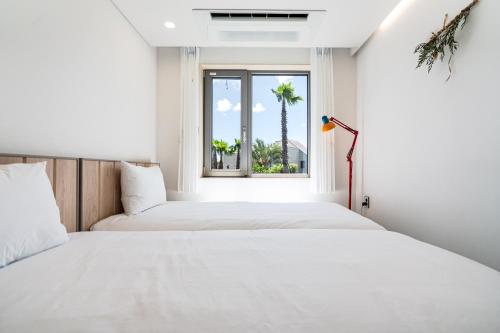 two beds in a room with a window and a palm tree at 제주살랑 in Tŏksu-dong