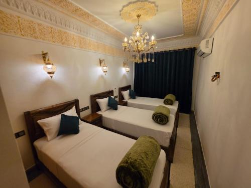 two beds in a room with a chandelier at Dar AWRABIA in Fez