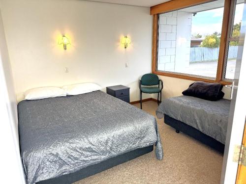 a bedroom with a bed and a chair and a window at Charlton Motel in Gore