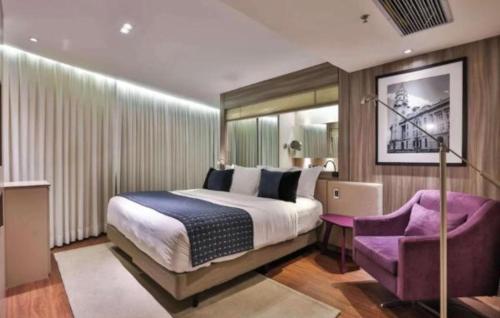 a bedroom with a large bed and a purple chair at Radisson V Olimpia in São Paulo