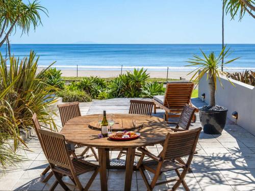 a wooden table and chairs on a patio with the beach at The Sands - Villa 28 - Stay Waiheke in Onetangi