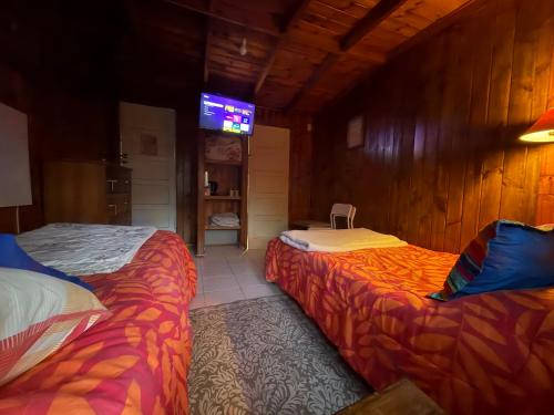 two beds in a room with a tv on the wall at Cabaña Los Corsarios in El Quisco