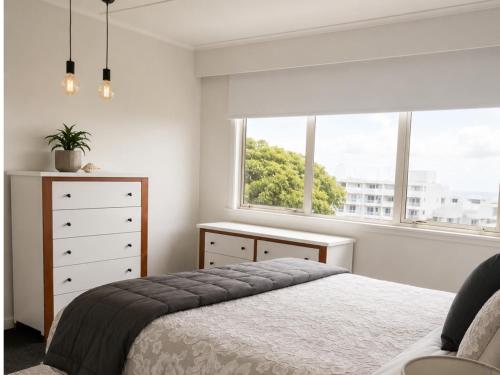 a bedroom with a bed and a dresser and a window at Bach By The Beach in Mount Maunganui