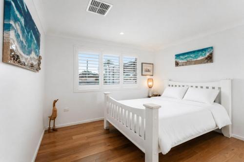a white bedroom with a bed and a window at Blue Summer House in Long Jetty