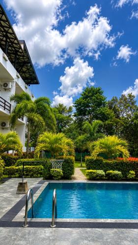 a swimming pool in front of a building with trees at River Bay Hotel in Pillagoda