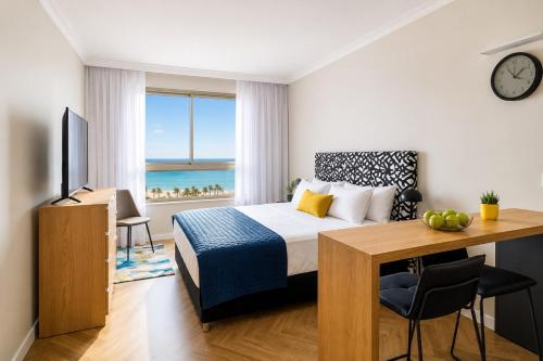 a bedroom with a bed and a desk and a window at מגדל אלמוג חיפה - דירות "בלו ביץ'" על הים in Haifa