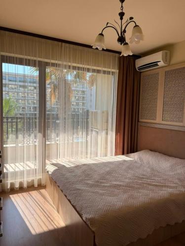 a bedroom with a bed and a large window at ЛУКСОЗЕН АПАРТАМЕНТ В 4 звезден хотел in Golden Sands
