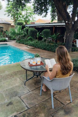 a woman sitting at a table reading a book at The Courtyard Guesthouse in Matola