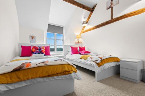 two beds in a white room with pink and orange at Traditional Cotswold escape with garden and fireplace in Cheltenham