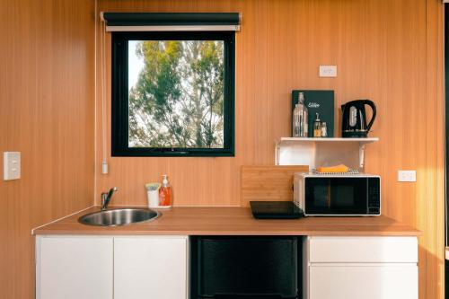 a kitchen with a microwave and a sink and a window at Raya and Aiden Farm House by Tiny Away in Cooma