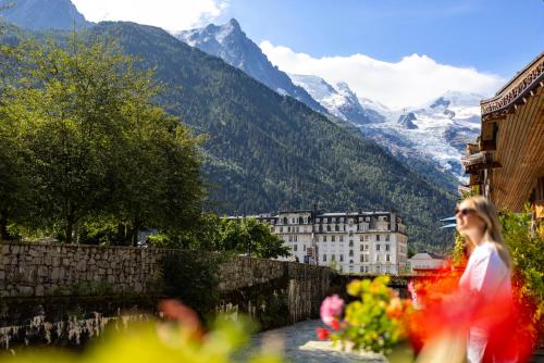 a woman walking past a building with mountains in the background at Hôtel de L'Arve by HappyCulture in Chamonix
